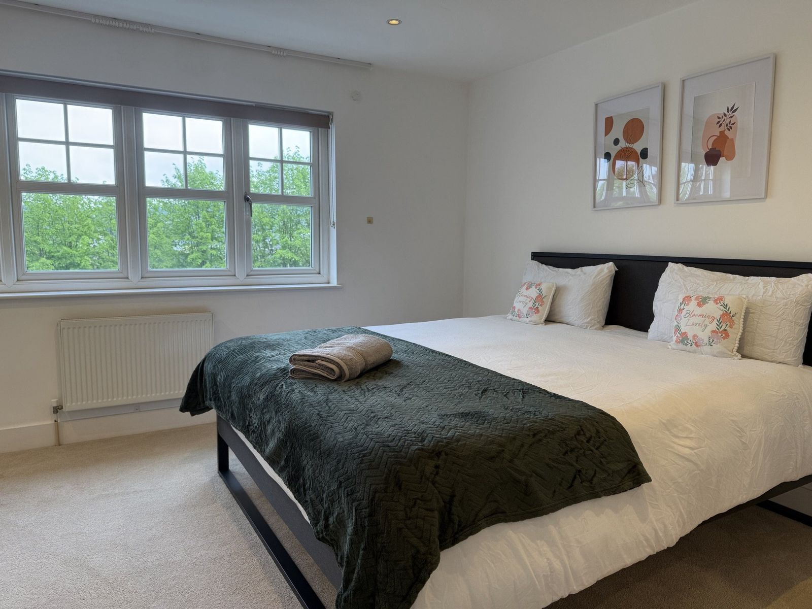 Second bedroom with green throw, botanical art prints, and white linens