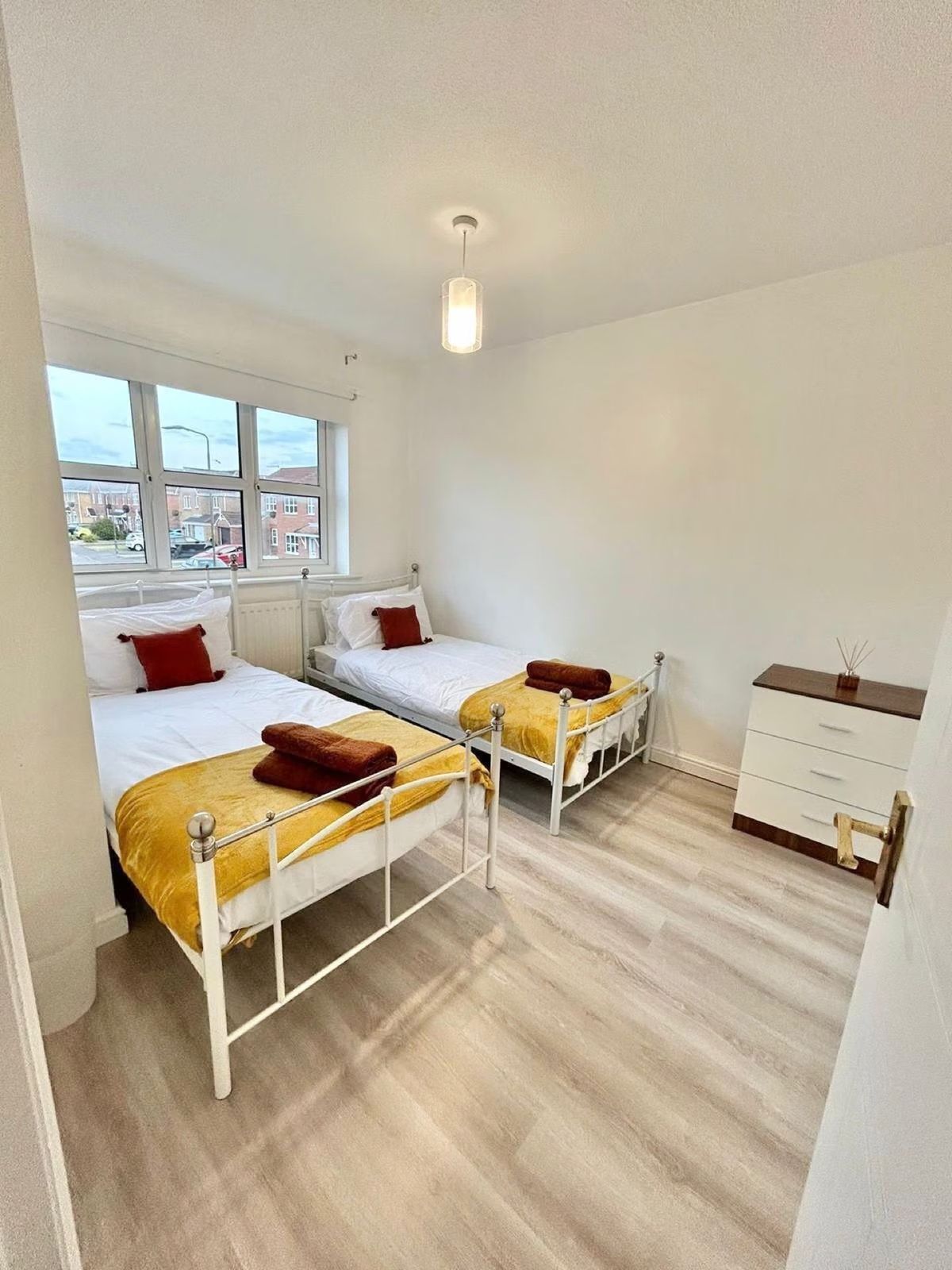 Second bedroom — two single beds with white frames and mustard accents, drawers, view to the front