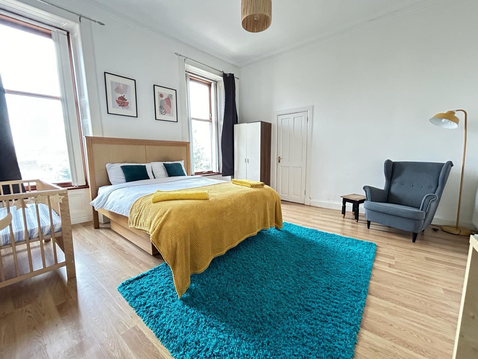 Master bedroom — alternative angle showing the cot, blue armchair, and tall windows